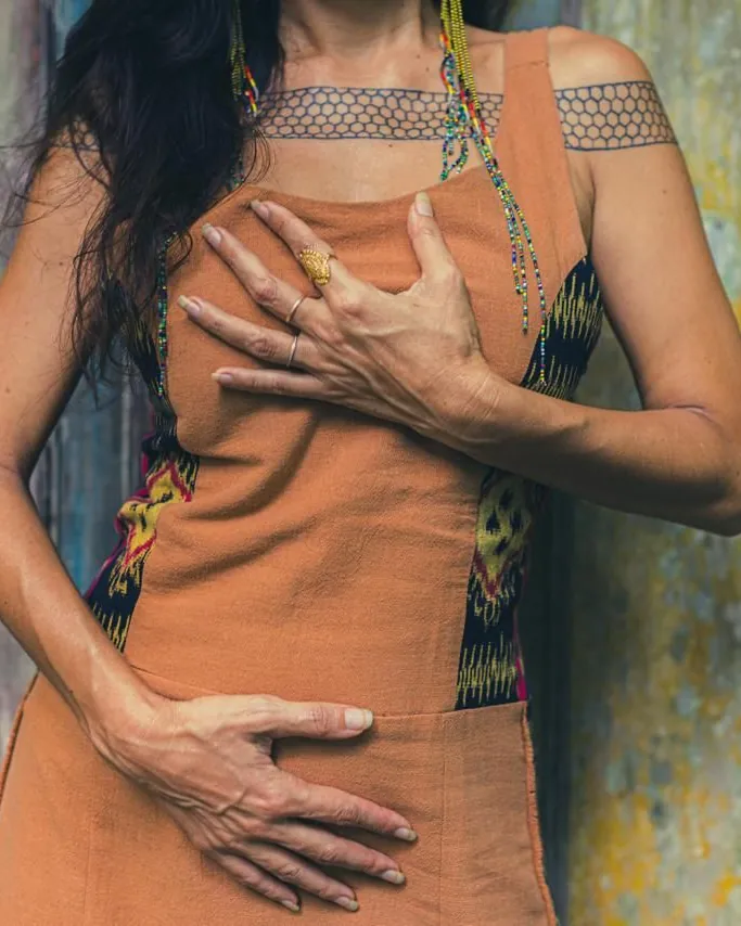 A woman in a terracotta dress resting one hand on her heart and the other on her womb